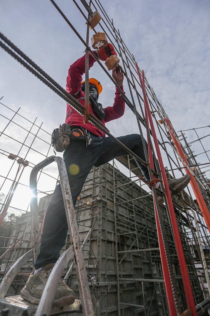 A construction worker wearing safety gear climbs a steel frame at an outdoor construction site.